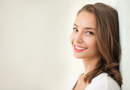 Young woman leaning against wall smiling with white teeth
