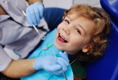 Child sitting in dental chair getting his teeth examined by a dentist