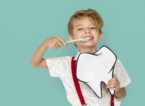 Boy holding paper toothbrush and giant paper tooth demonstrating how to brush